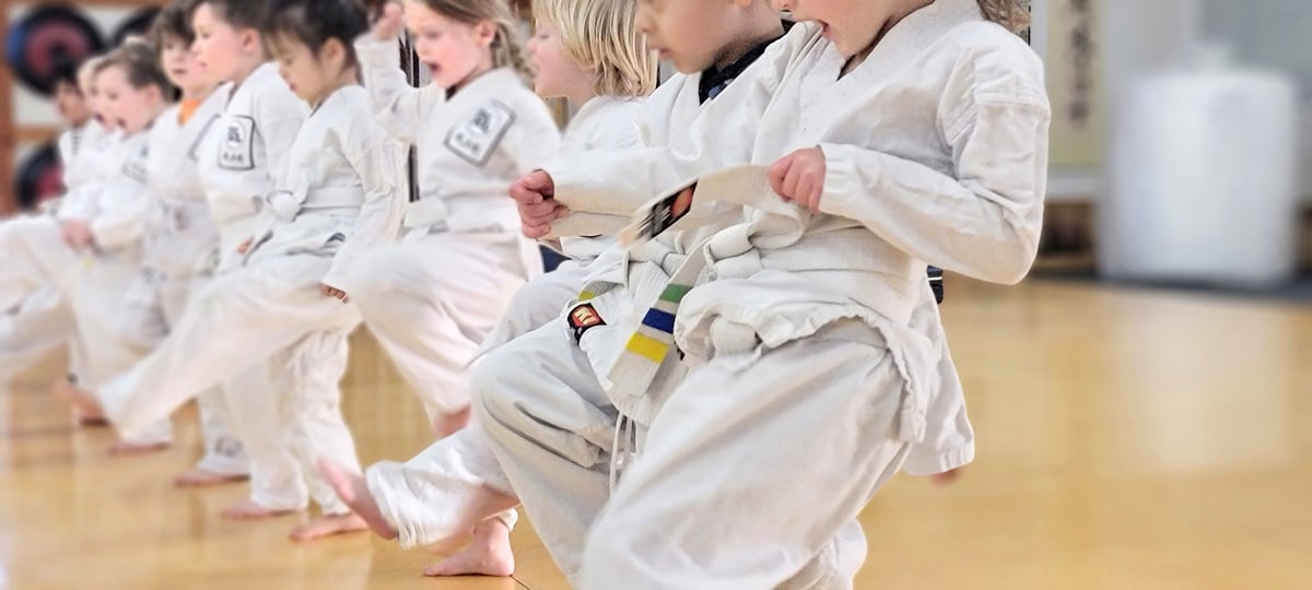 a group of children doing kicks in white karate uniforms