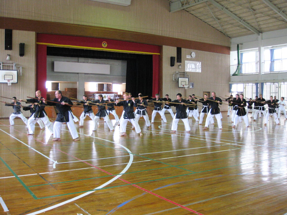 a group of people practicing kobudo weapons in a gym in Okinawa